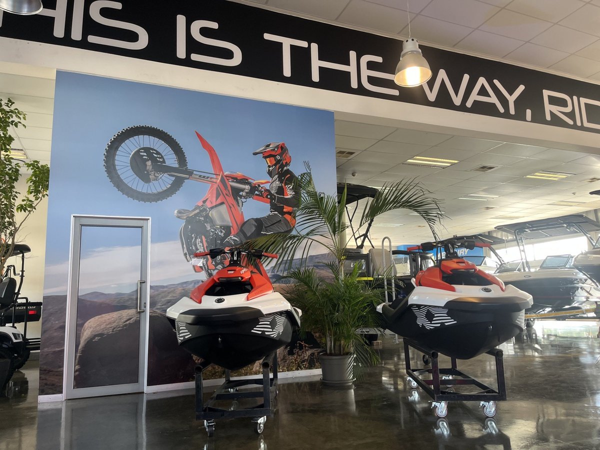 Full-height custom printed wallpaper mural installed in a powersports showroom, with a motocross rider in mid-air above red and black jet skis, Imagine Graffix Pretoria