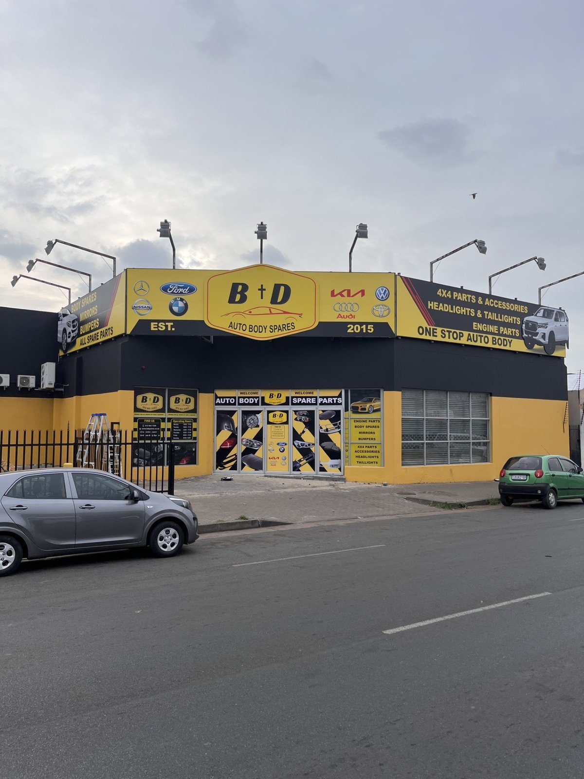Full building banner wrap on the B and D Auto Body Spares shopfront, showing large-format PVC banner panels with brand logos, product imagery and contact details, an example of outdoor banner printing by Imagine Graffix in Pretoria